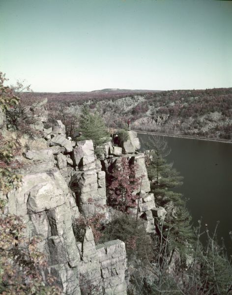 Elevated view of Devil's Lake and surrounding area from a bluff on the east side of the lake. A man is standing on top of the rock formation near the center of the image.