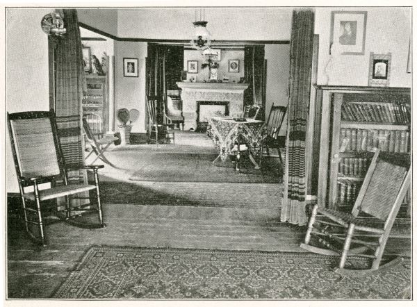 The parlors at Hillside Home School, featuring a fireplace, bookshelves, curtained doorways, and rocking chairs.
