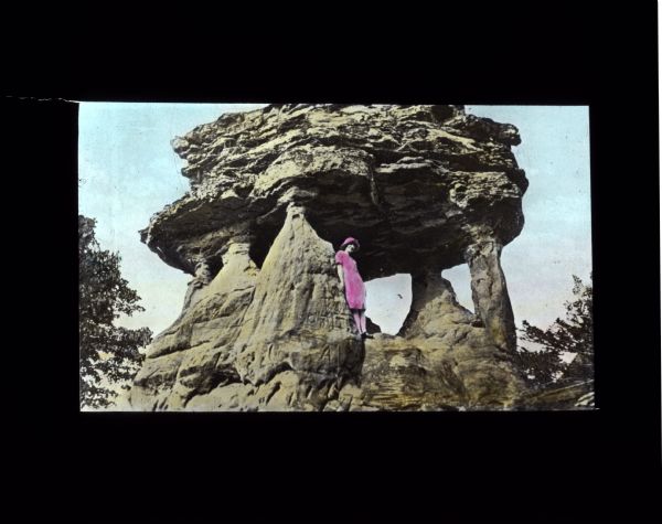 View uphill towards a woman posing on a large, exposed rock formation.