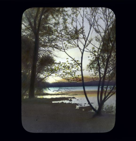 View between trees from Willow Drive of the sun setting over Lake Mendota. 