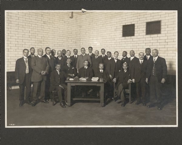 Group portrait of men in the Pullman Porter's Union posing indoors. A group of men are standing around five men sitting around a table.