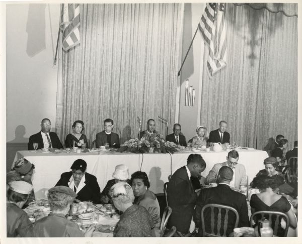 Elevated view over people sitting at tables in front of the head table, at the NAACP Milwaukee Branch's 1958 Annual Dinner. Roy Wilkins, seated in the middle of the head table, was the guest speaker.
