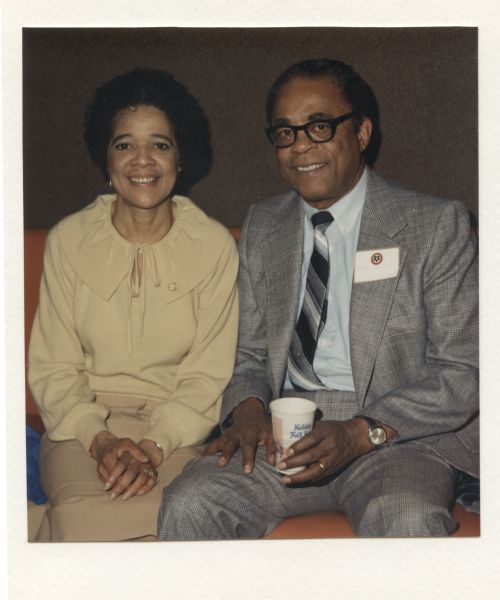 Vel Phillips sitting with her husband W. Dale Phillips, who is holding a cup that says "Holiday Folk Fair." This image is affixed to a holiday card Vel and Dale received from Erol Reyal. The note in the card reads: "It was a pleasure meeting you both at this years (<i>sic</i>) Holiday Folk Fair. Have a Happy New Year and keep smiling. Yours Truly, Erol Reyal & Cilento Studios."