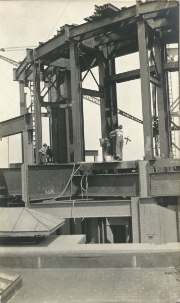 Construction of the dome for the Fourth Wisconsin State Capitol building. Four men are at working around the girders of the dome. One man is marked with an "X" drawn in pen. Caption on the back reads: "Superstructure of dome proper at the 106' level. Alex Doyle caught as he was throwing a rivet."