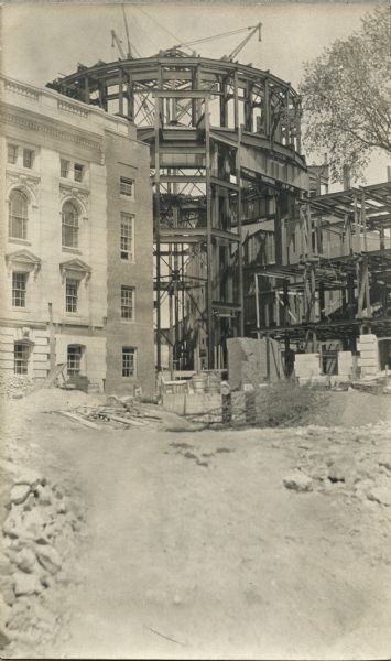 View from ground towards the construction of the dome for the fourth Wisconsin State Capitol building. The 1904 fire that destroyed large sections of the third Capitol building made the fourth building necessary. The fourth Capitol building had to be undertaken in sections over many years, due to financial constraints and the need for parts of the building to remain open for government work. Caption on back of image reads: "Substructure of dome and the first 50' of dome proper. Showing corner of south wing and the substructure and superstructure of dome up to 106' level."