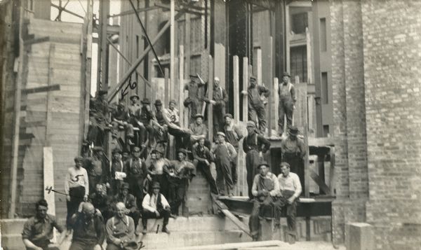 Group portrait of construction workers for the dome of the fourth Wisconsin State Capitol building. In total thirty-two men are posing, with six of the men marked with numbers drawn in pen. Caption on back reads: "Gang of structuralism workers erecting the superstructure of the new dome of the Wis State Capl Bldg. 
#1 - C W Hamilton (Draft.)
#2 - Dan McKee (foreman)
#3 - Al Long (rivet foreman)
#4 - A Dawson (foreman)
#5 - C W George (time keeper)
#6 - (Smity) F E Smith. The <u>goat</u> of the bunch. Killed May 30, '11, by falling from erection tower 241 feet."