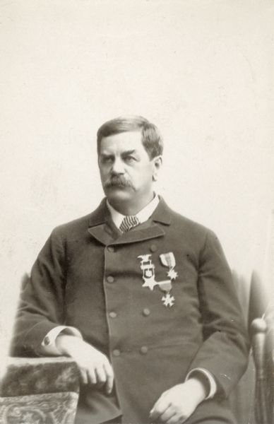 Waist-up portrait of William Upham, sitting in a chair with his arm resting on a table. He has three medals pinned to his coat.