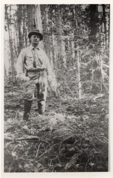 Informal portrait of Frederick Jackson Turner standing in the woods on a camping trip.