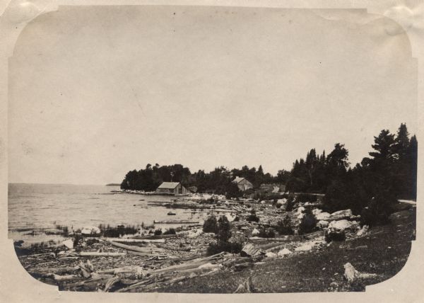 View along shoreline of Weborg Point before the area became Peninsula State Park. Green Bay is on the left. Two wood buildings are along the shoreline in the center.