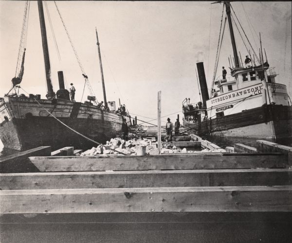 Two ships docked in a Door County harbor, possibly at Sturgeon Bay. The ship at left is the <i>Oak Leaf</i>. The ship at right is the <i>L.N. Foster</i> owned by Sturgeon Bay Stone Co.