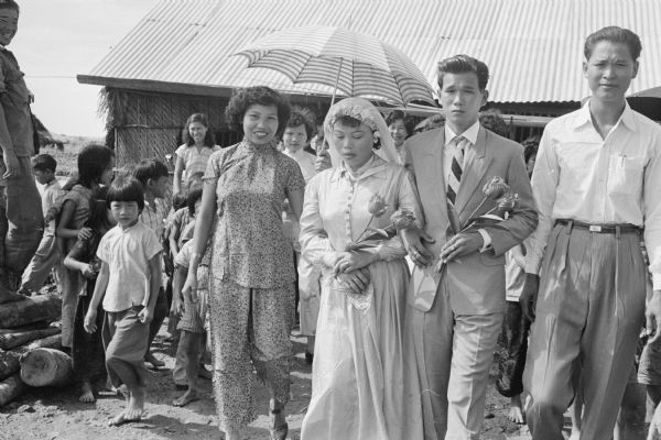 The bride Anh Le Vuong and groom Tien Vinh Le at their wedding in Binh Hung, Vietnam. Their attendants are at their sides. The woman next to Vuong is holding a parasol.