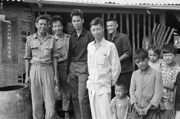Group portrait of Vietnamese men and children standing outdoors, who have probably gathered for the wedding of Anh Le Vuong and Tien Vinh Le in Binh Hung, Vietnam.