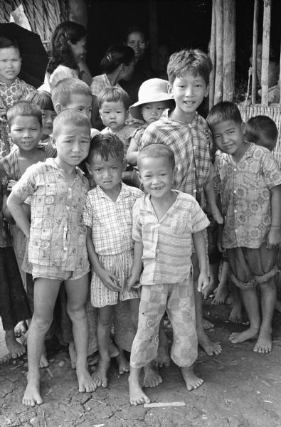 Group portrait of children who are probably gathered to attend the wedding of Anh Le Vuong and Tien Vinh Le in Binh Hung, Vietnam. Women are standing in the background.