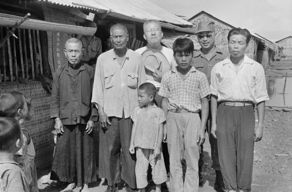 Outdoor group portrait of Vietnamese men and several children. They are probably gathered to attend the wedding of Anh Le Vuong and Tien Vinh Le in Binh Hung, Vietnam. The man wearing sunglasses standing second from the right is wearing a military uniform.