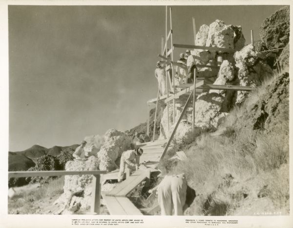 Workmen building a wooden walkway and platform around a cliff for the film "Wuthering Heights."