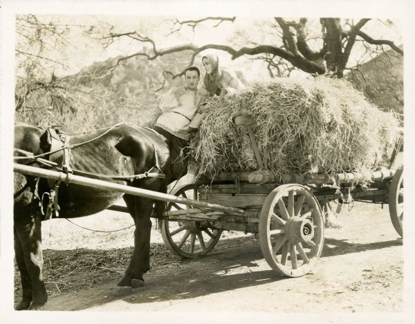 Prince Dimitri (Rod La Rocque) standing on a wagon of hay drawn by a horse. Katusha Maslova (Delores del Rio) is sitting on top of the hay. The still is from the film "Resurrection."