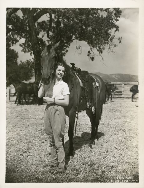 Mae Jackson (Betty Field) standing with a horse and holding its bridle on the set of the film "Of Mice and Men."
