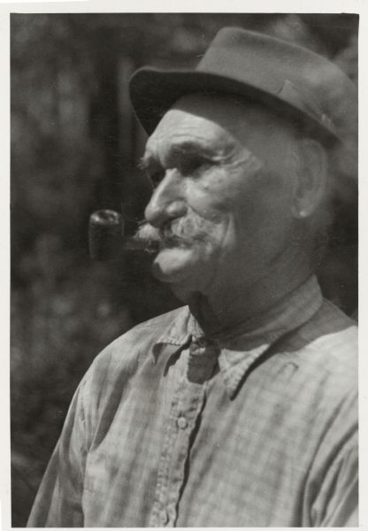 Quarter-length portrait of Antoine Dennis smoking a pipe.