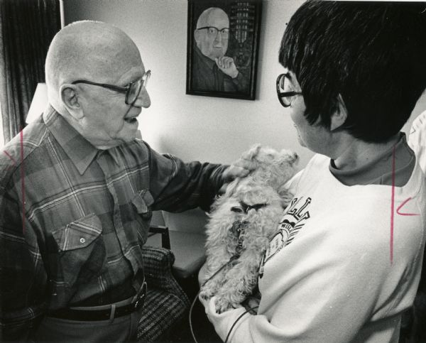 A smiling man is petting a dog held by a woman. Caption reads: "Art Borowiak patted Buttons, a toy poodle owned by Ann Turney."