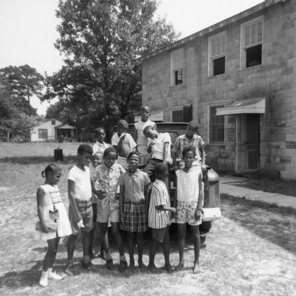 A group of African-American children pose outdoors on and in front of a pickup truck during Freedom Summer.  Likely at the Freedom School, Priest Creek Baptist Church.