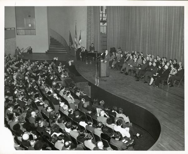 A view from a balcony of Reinhold Neibuhr at a podium on a stage, speaking to a seated audience. This is probably at an event for Americans For Democratic Action.