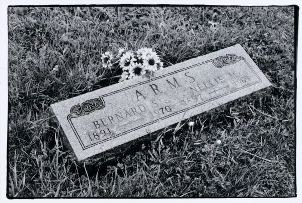 A rectangular gravestone bearing the birth and death years of Bernard and Nellie Arms. There are flowers next to the stone.