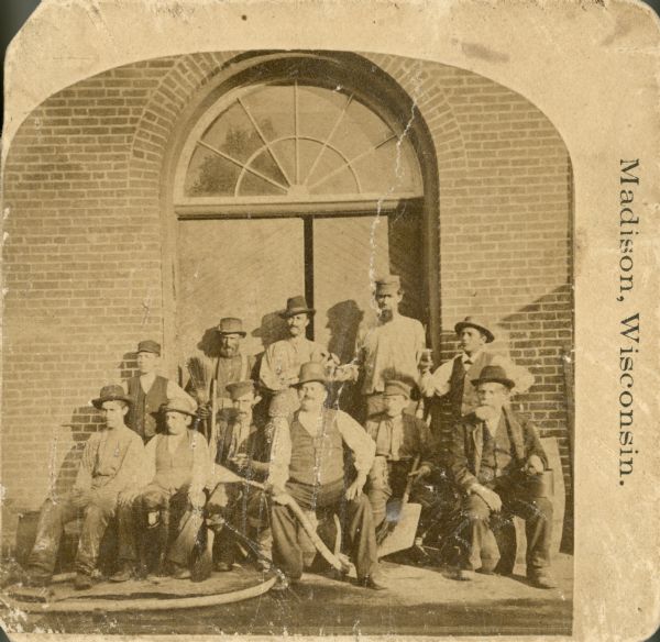 A group of men posing together at Fauerbach Brewing Company. They are probably brewery employees. The man seated front and center on a barrel, holding a beer hose is probably brewmaster Peter Fauerbach.