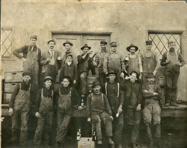 Group portrait of brewery employees at Fauerbach Brewing Company. Most of the men are wearing coveralls and holding bottles of beer.