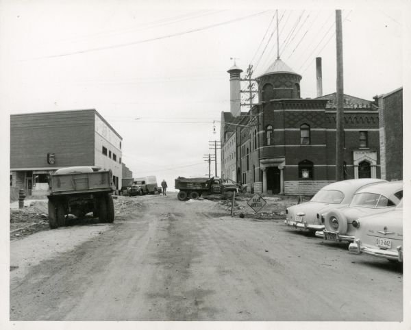 View up street, with the Fauerbach brewery in the background on the right. Several cars and trucks are parked on the sides of the street in the foreground.