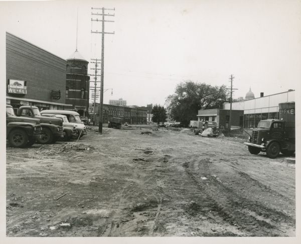 View of the area behind the Fauerbach brewery. There is a Wil Kil sign on the building on the left. The dome of the Wisconsin State Capitol can be seen on the right. Several vehicles are parked in this area.