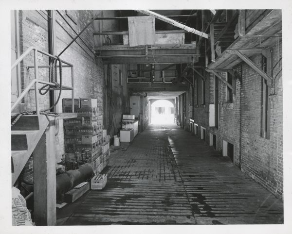 View down a large passageway inside the brick brewery. There are cases of beer stacked against the wall, and a small stairway on the left. 