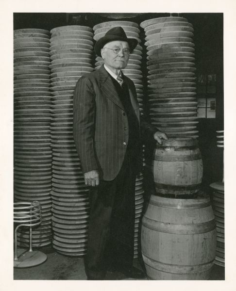 A portrait of Frank Hess of Hess and Sons Cooperage. He is wearing a suit and posing with wooden barrels.
