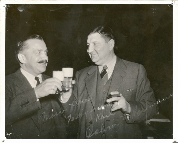 Calvin Kaufmann (left) of Stevens Point Brewery and Karl Fauerbach toast with glasses of beer. Fauerbach is holding a cigar. The photograph is autographed by Kaufmann with the sentiment: "Merry Xmas to my friend Karl. Calvin Korfmann."