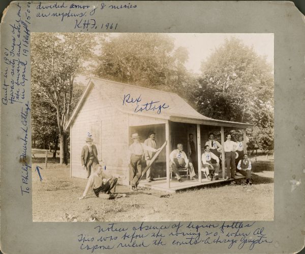 A group of friends gathered outside the Rex Cottage. Identified by written numbers are 1. George Beschoff 2. Ed Biggleson 3. Adolf Wagner 4. William Lee 5. Philip Fauerbach 6. Carl Yaeger/Jaeger 7. Robert Schmedeman. Karl Fauerbach wrote more information on the photograph in blue ink, including this caption: "Notice absence of liquor bottles. This was before the roaring 20s when Al Capone ruled the (illegible)--a Chicago gangster."