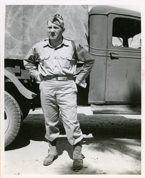 Portrait of Robert Allen standing next to a truck, wearing military fatigues and with his hands on his hips.