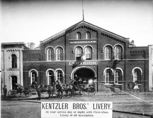View from across street towards the Kentzler Brothers Livery. Kentlzer was at 107-11 E. Doty Street. There is a wagon with a driver and four horses directly in front of the large arched open doorway. To the left and right are carriages. Printed at the bottom: "At your service day or night with First-Class Livery of all description."