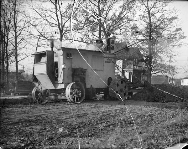 A Harnischfeger Corporation #14 KW machine creating a trench. The title caption gives the trench measurements as 22" x 5 1/2'. There is a house in the background.