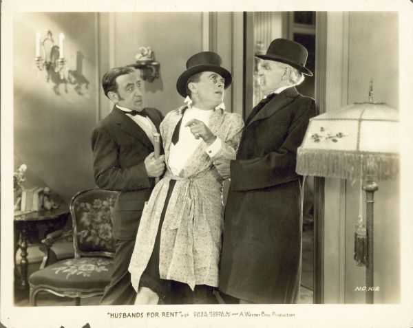 Sir Reginald Knight (Claude Gillingwater) and another man holding Herbert Willis (Owen Moore) by the arms. Knight is looking angrily at Willis who is wearing a robe over his tuxedo in a still for the 1927 film "Husbands for Rent."