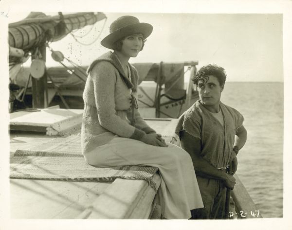 Reginald Jones (George Walsh) gazing up at Helen Lattimore (Florence Dixon) in a scene from the 1919 film "Never Say Quit." The two are on a yacht, and she is sitting slightly above where he is standing.