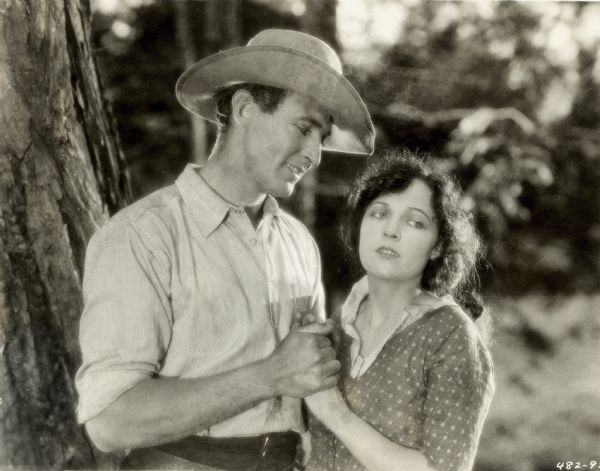 Jacqueline Logan and Maurice Flynn holding hands in a still from the film "Salomy Jane." Flynn is looking lovingly at Logan while she is looking somewhat worried off to the side.