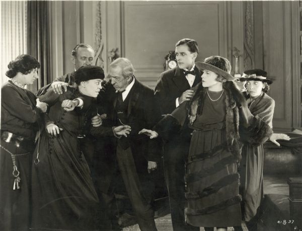 Three men restraining a woman in a still from the film "For the Defense." Another woman and a man are shielding a third woman.