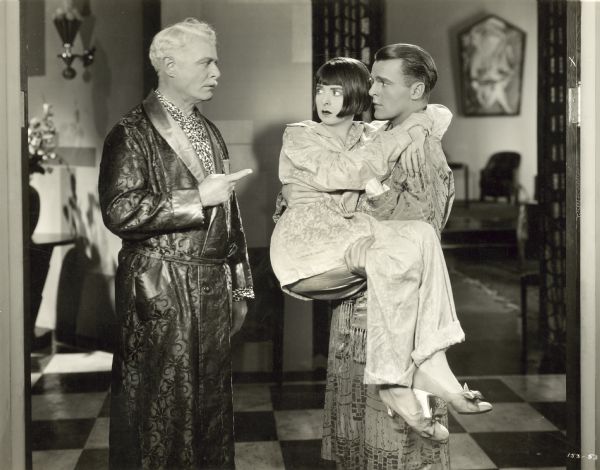 Edward Martindel confronting Neil Hamilton who is holding Colleen Moore in a still from the film "Why Be Good?" All three are dressed in pajamas and robes.