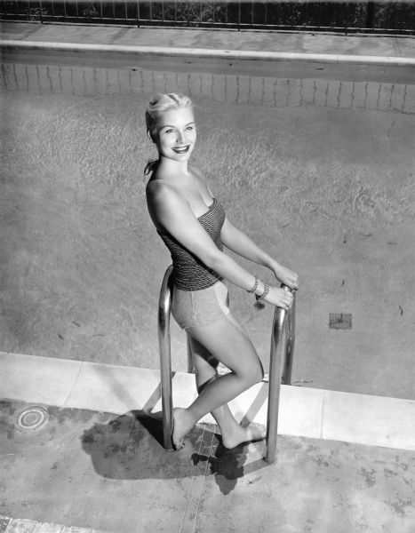Barbara Payton posing for a publicity photograph for the film "Trapped."  She is standing on the pool deck in between the hand rails for the pool ladder.