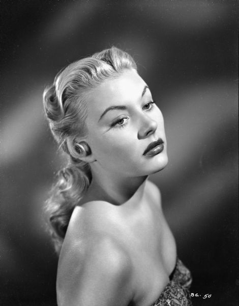 Publicity still of Barbara Payton for the film "Bride of the Gorilla." She is wearing a sleeveless gown. Her head is tilted up and she is looking downward.