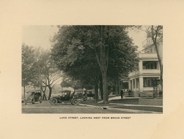 A view of Lake Street, looking West from Broad Street. Hotel Lane is on the right side, and several automobiles are parked backed-up to the curb in front.