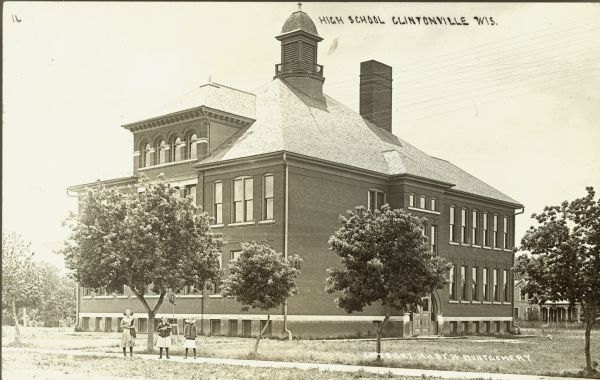 View from street of the high school. Three girls are standing on the sidewalk in front of the school. Caption reads: "High School, Clintonville, Wis."