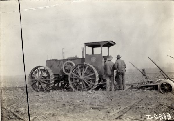 Two men are standing next to the back of an International Harvester four wheel drive tractor in a field.