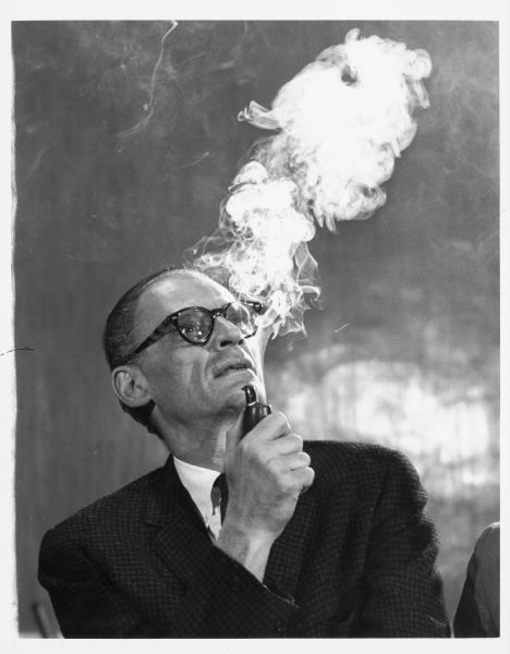 Quarter-length portrait of Arthur Miller smoking a pipe while at a rehearsal for the play "After the Fall."