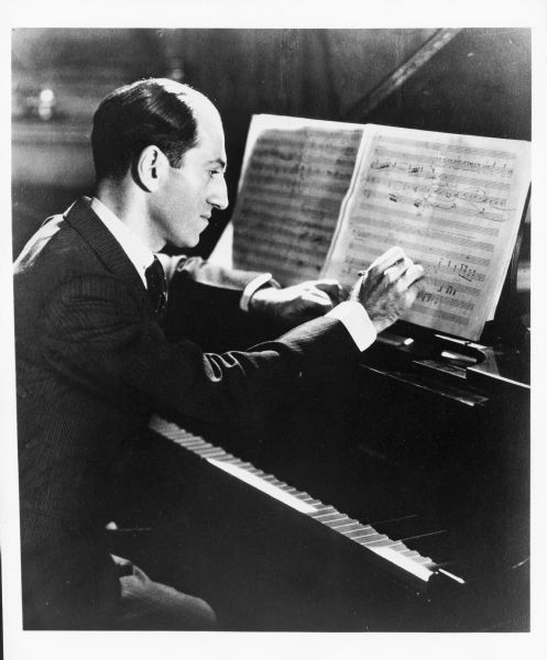 Portrait of George Gershwin sitting at a piano and working on a score.