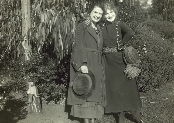 Florence Lawrence and her mother Lotta are standing together outdoors wearing overcoats and holding their hats. They are both smiling, and Florence has one arm around her mother's neck.  